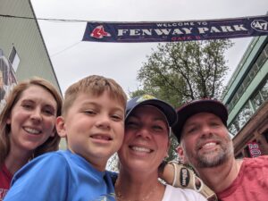 Three smiling adults and one child stand under a Fenway Park banner